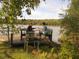 Kuvassa Keitaanjärven mysteerejä pelataan Rymättylässä veden äärellä. Kaksi hahmoa on laiturilla punomassa suunnitelmia. Päivä on aurinkoinen, vain muutamia valkoisia pilvenhattaroita.